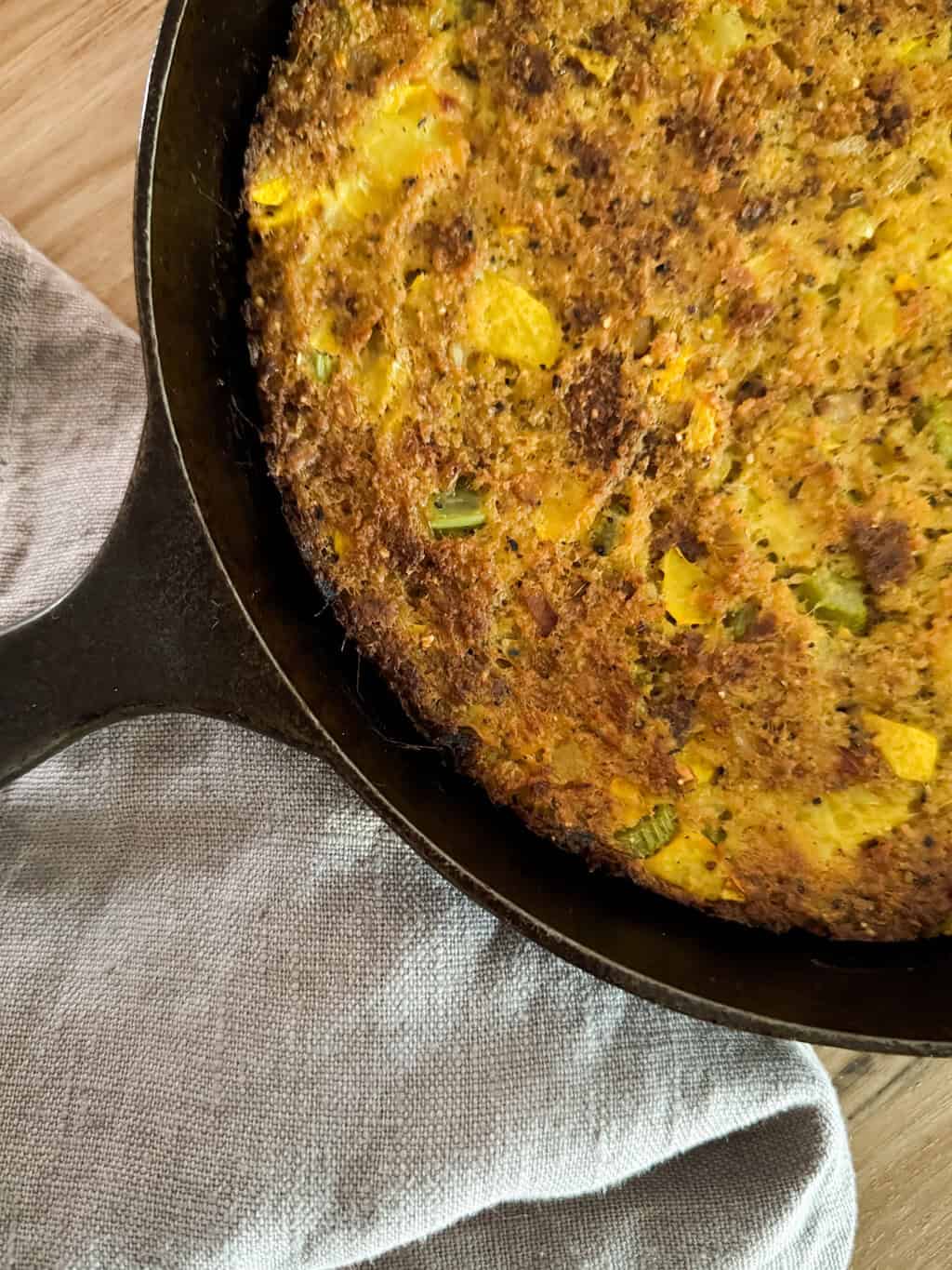 Southern Yellow Squash Cornbread Dressing baked in cast iron skillet with golden-brown crispy top, served with gray linen napkin on wooden surface