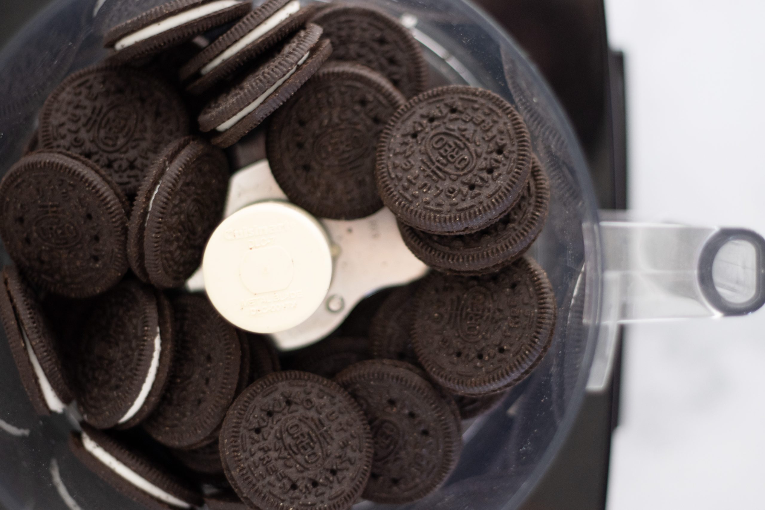 A food processor filled with whole Oreo cookies, ready to be pulsed into fine crumbs for a no-bake crust.