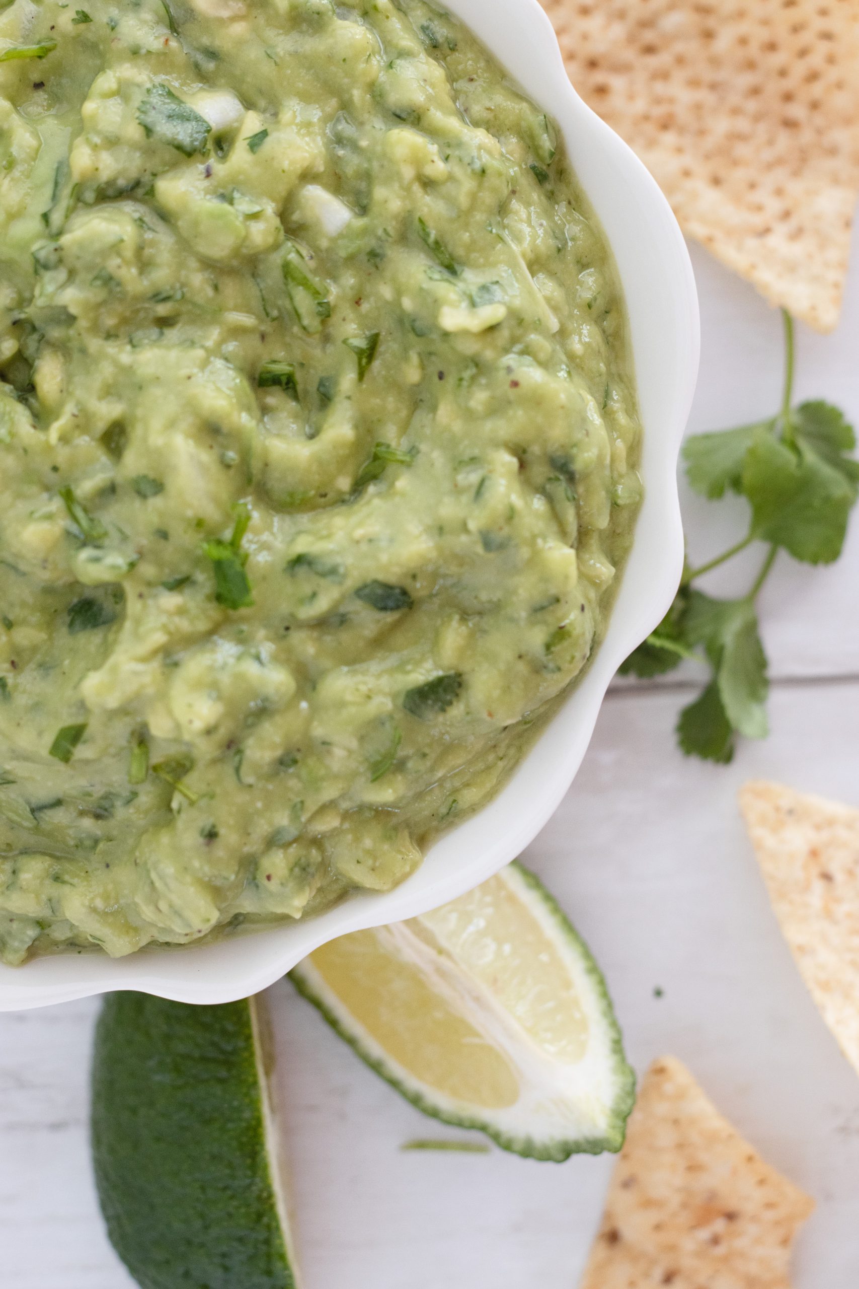 A bowl of creamy homemade guacamole with fresh cilantro, and a squeeze of orange and lime juice, served with tortilla chips.