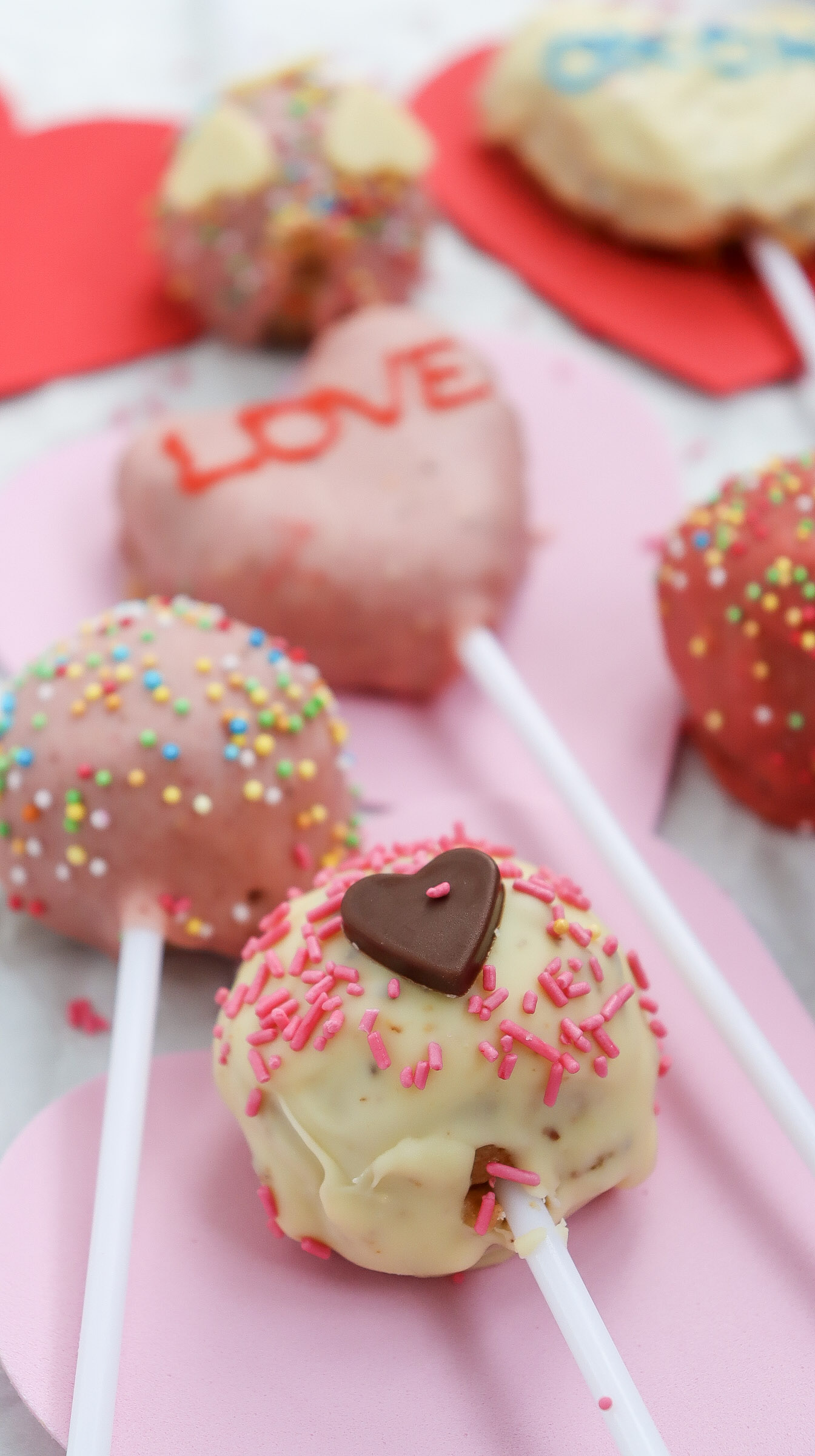 A collection of beautifully decorated Valentine’s cake pops coated in chocolate and topped with sprinkles and drizzled chocolate.