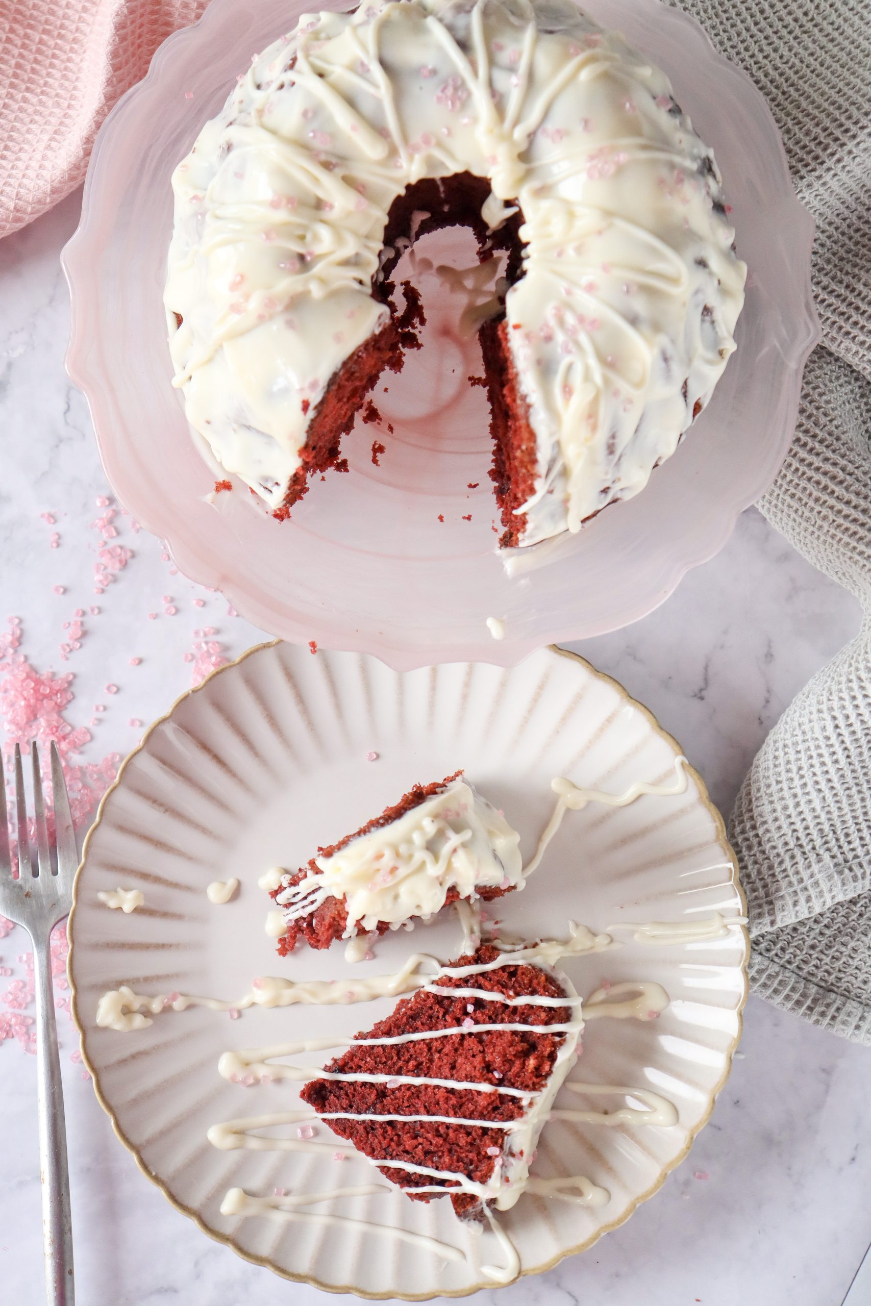 A whole red velvet Bundt cake topped with a thick cream cheese glaze, displayed on a rustic cake stand.